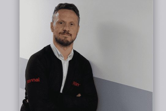 Chris Goggin of Rinnai, in a dark Rinnai-branded top, against a white wall.