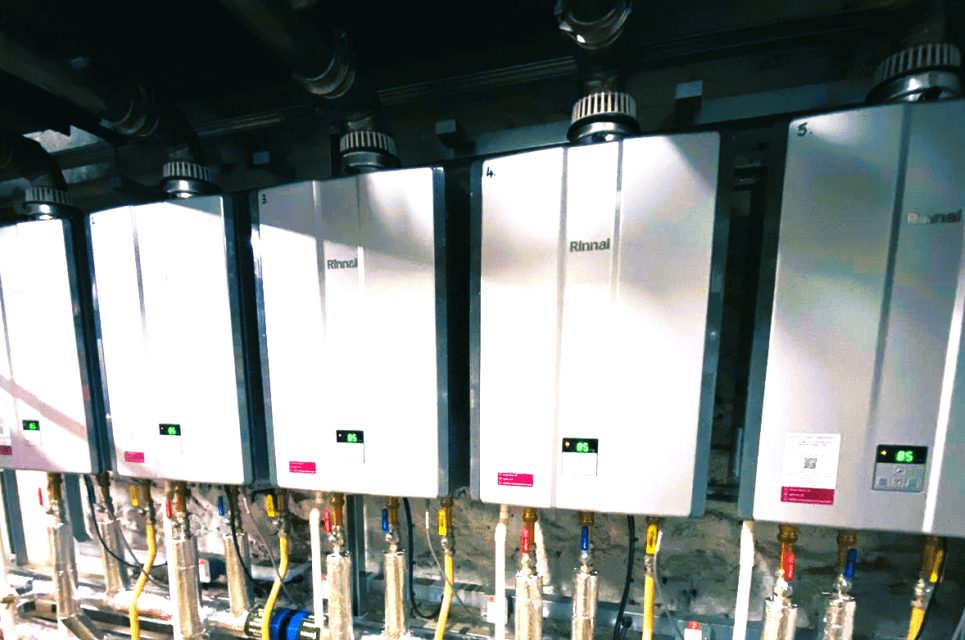 A row of Rinnai continuous-flow water heaters mounted on a plant room wall.