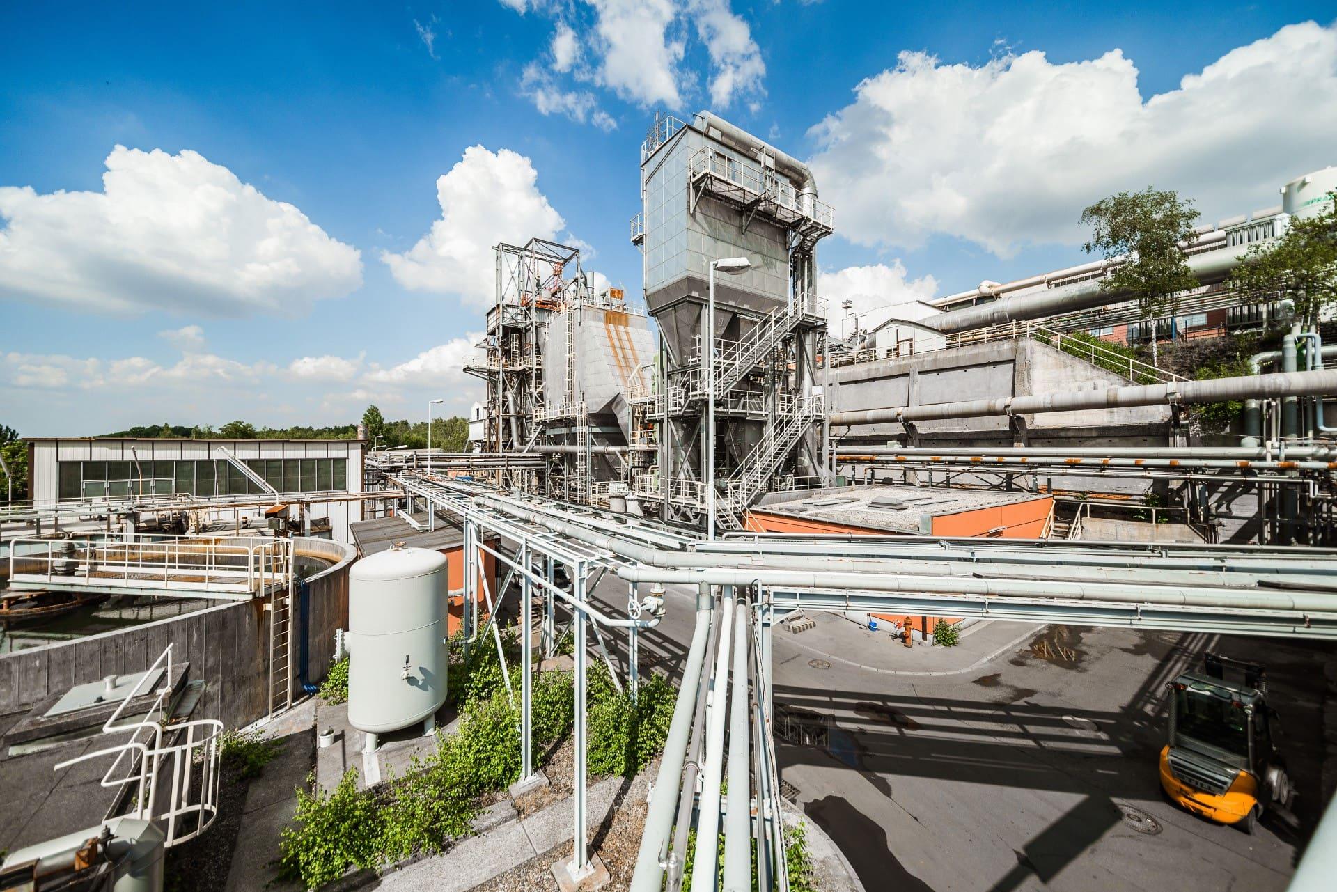 An Ecobat battery recycling plant with pipework and processing towers under a blue sky.
