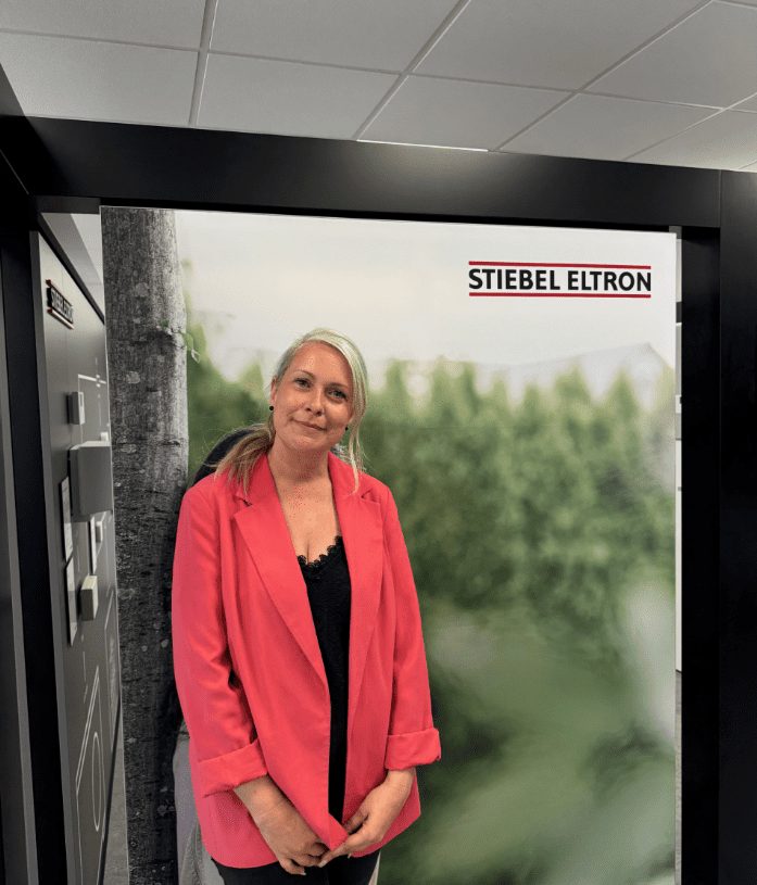 Claire Poole of Stiebel Eltron, in a pink jacket, standing in a doorway at a Stiebel Eltron display.