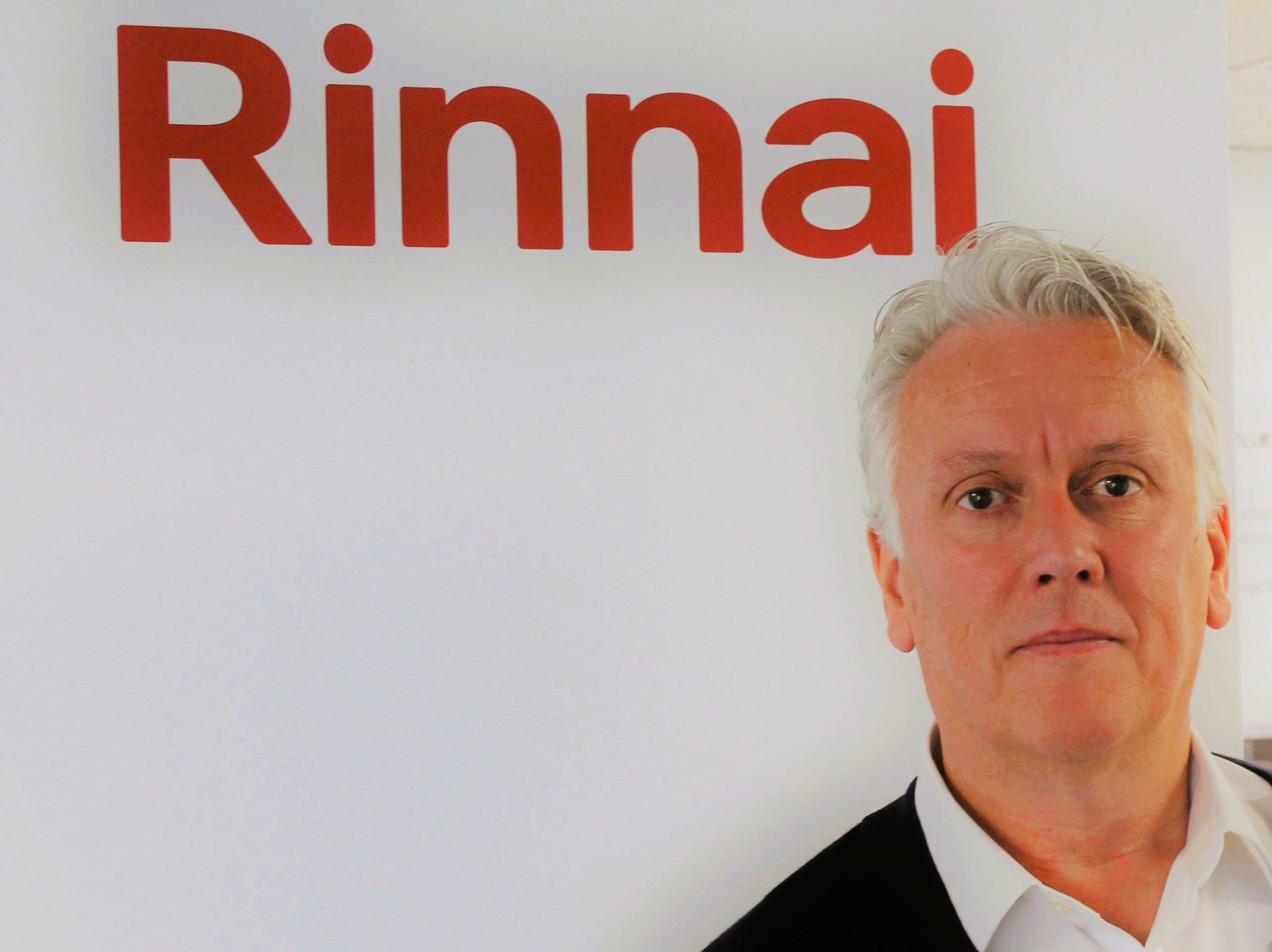 Tony Gittings of Rinnai in front of a wall with the Rinnai logo.