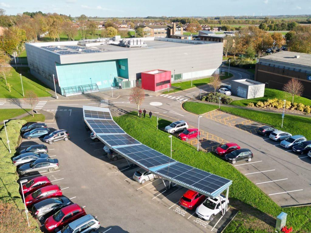 Aerial view of a car park with a solar carport beside a large office building.