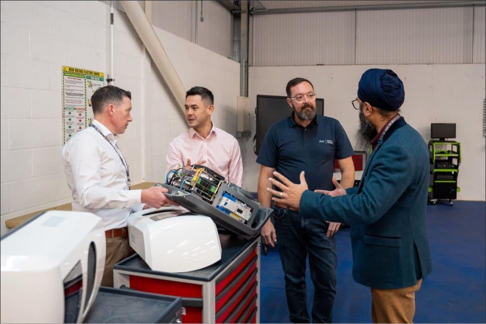 An instructor shows students an EV component on a workbench in a college training workshop.