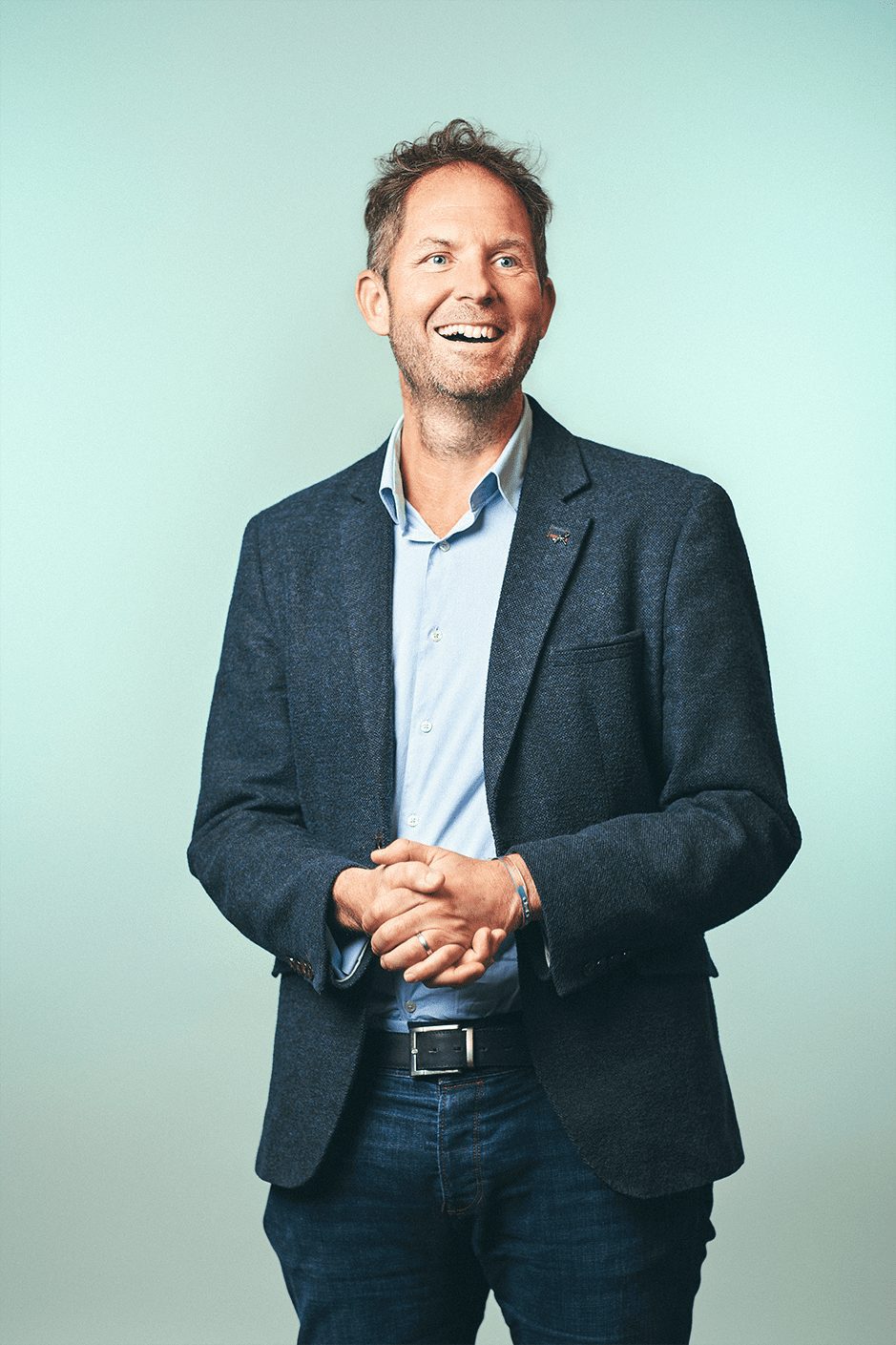 Alex Warren of Stark, smiling, in a navy jacket against a pale green background.