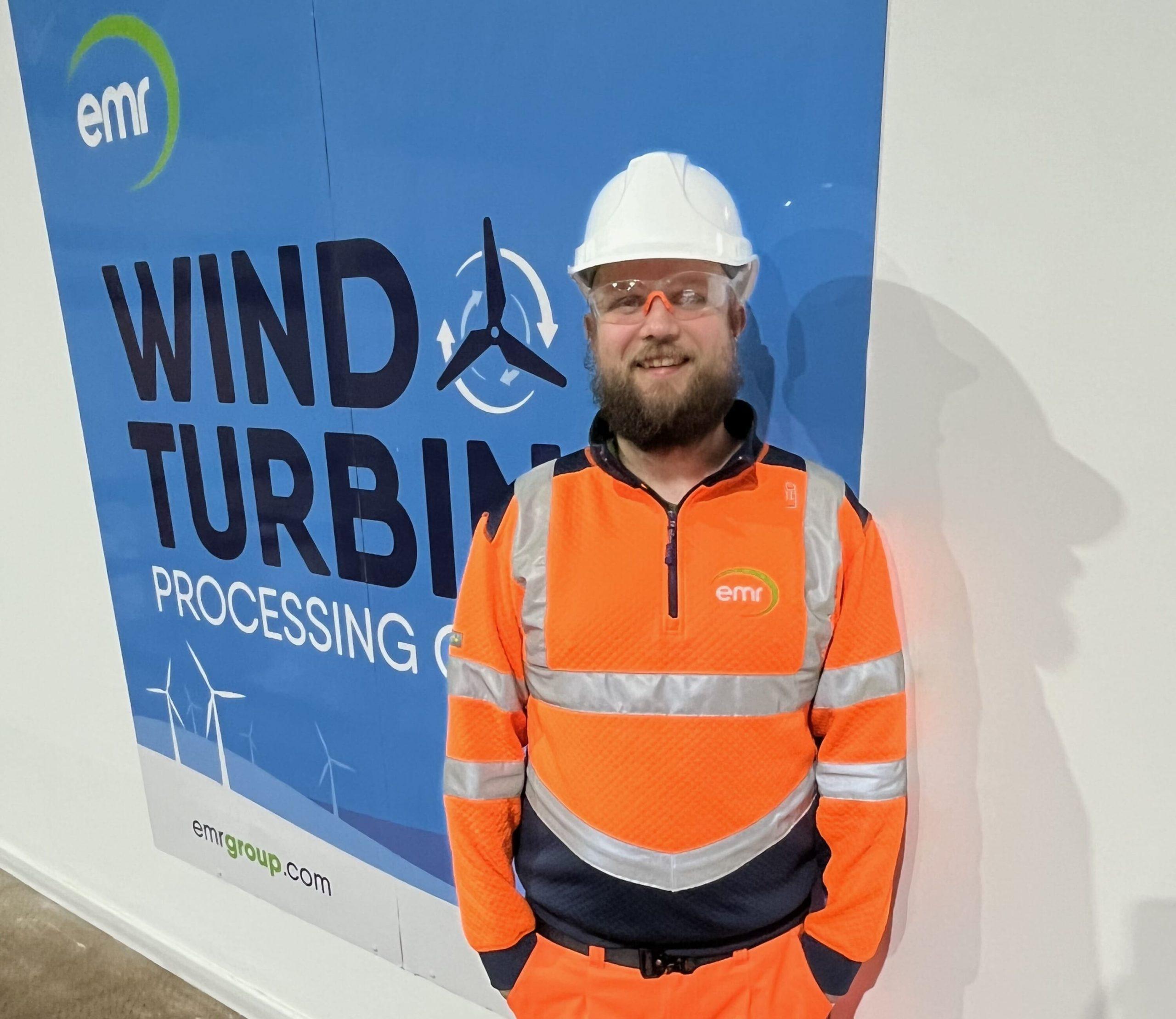 Andy Hearl of EMR, in a hard hat and orange hi-vis, in front of a Wind Turbine Processing sign.
