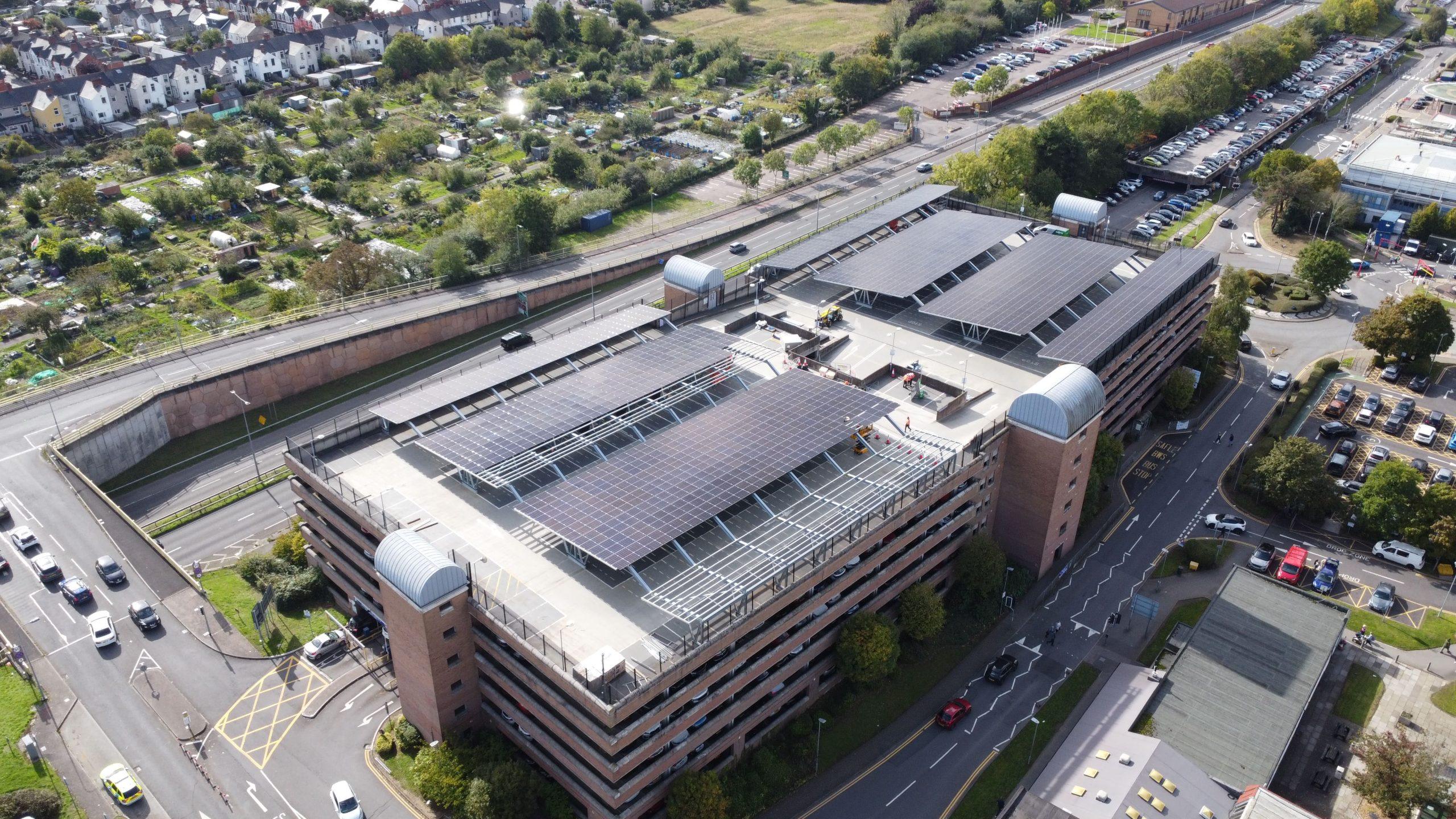 Aerial view of a hospital car park covered by solar carports, beside the hospital buildings.