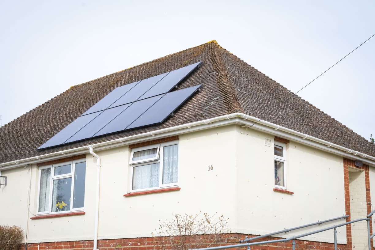A council house with solar panels on its roof, under a grey sky.