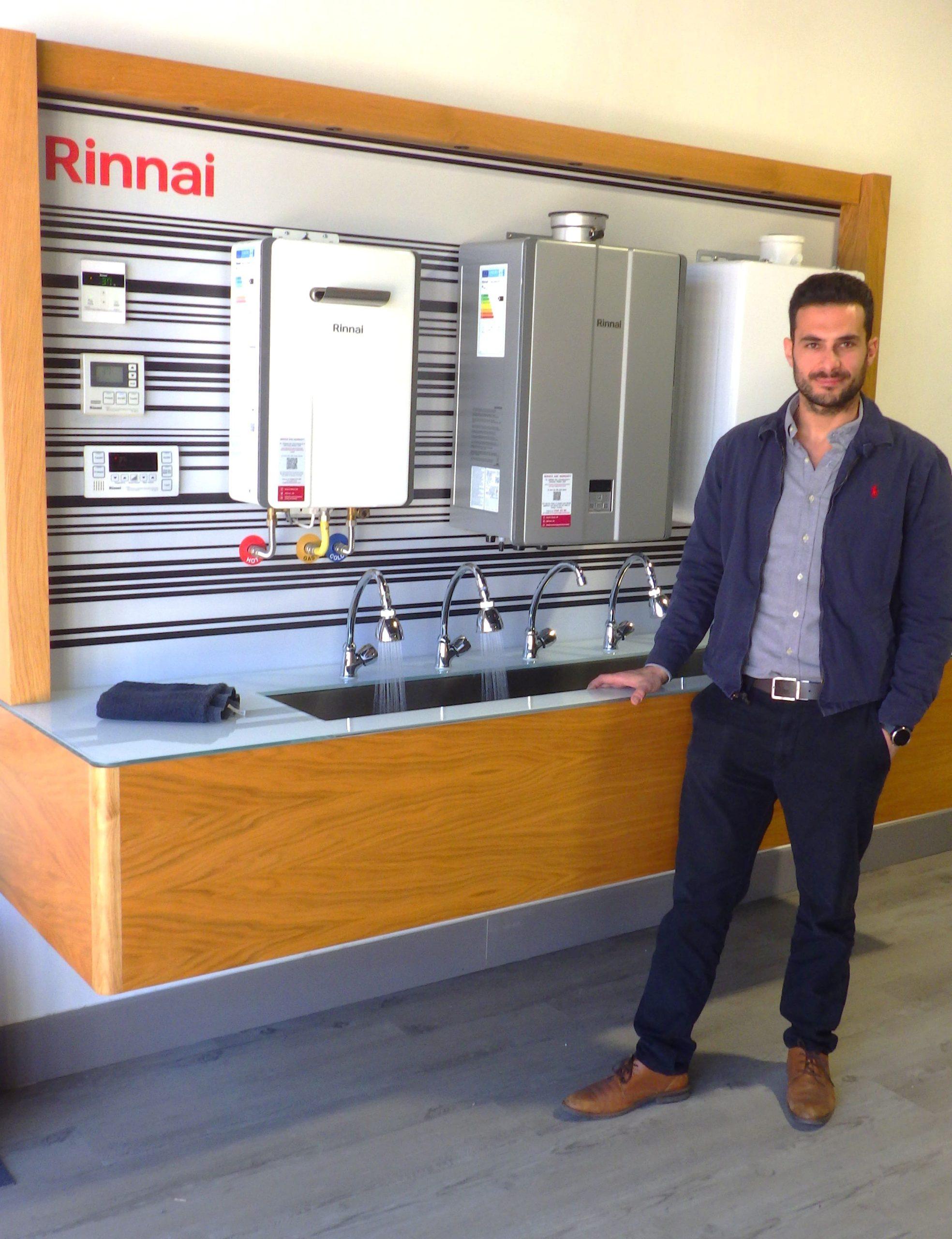 A man stands in front of a Rinnai water heater display wall in a showroom.