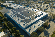 Aerial view of a large commercial building with solar panels covering its flat roof.