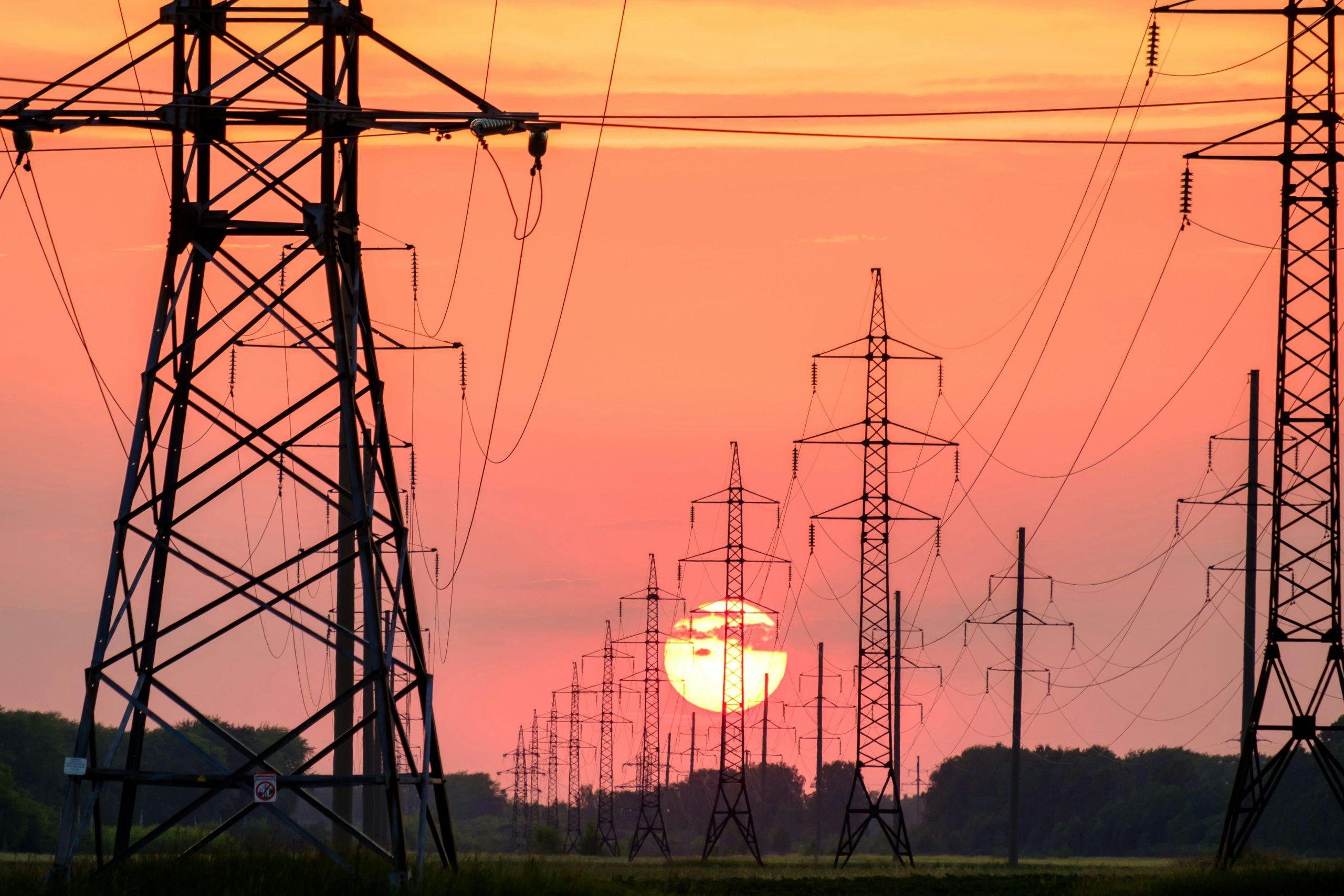 Electricity pylons and power lines silhouetted against a red sunset.