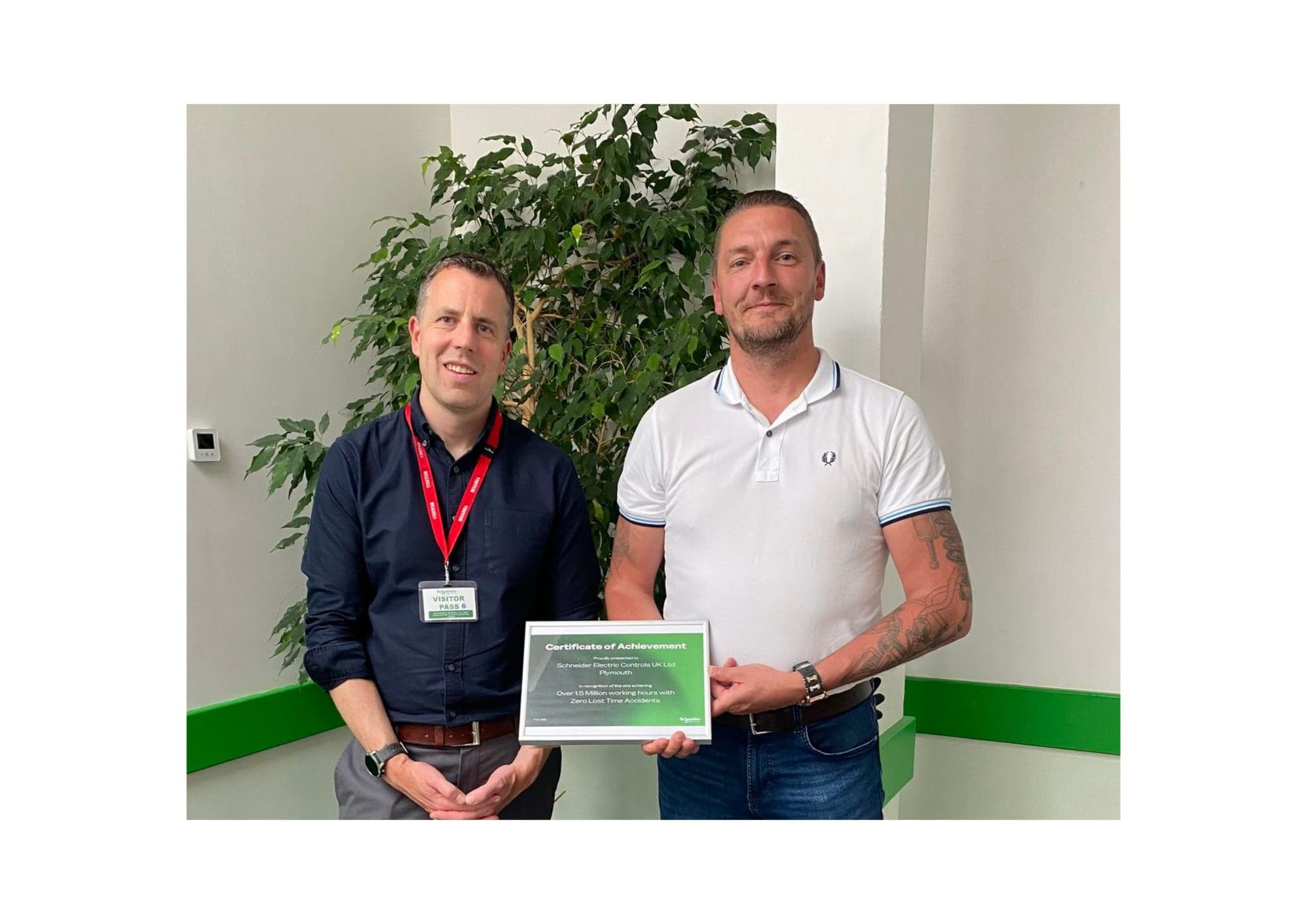Two men stand in an office holding a certificate between them.